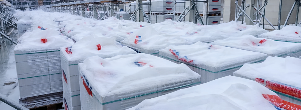 Verpakte kalkzandsteenpakketten in de sneeuw op de bouwplaats.