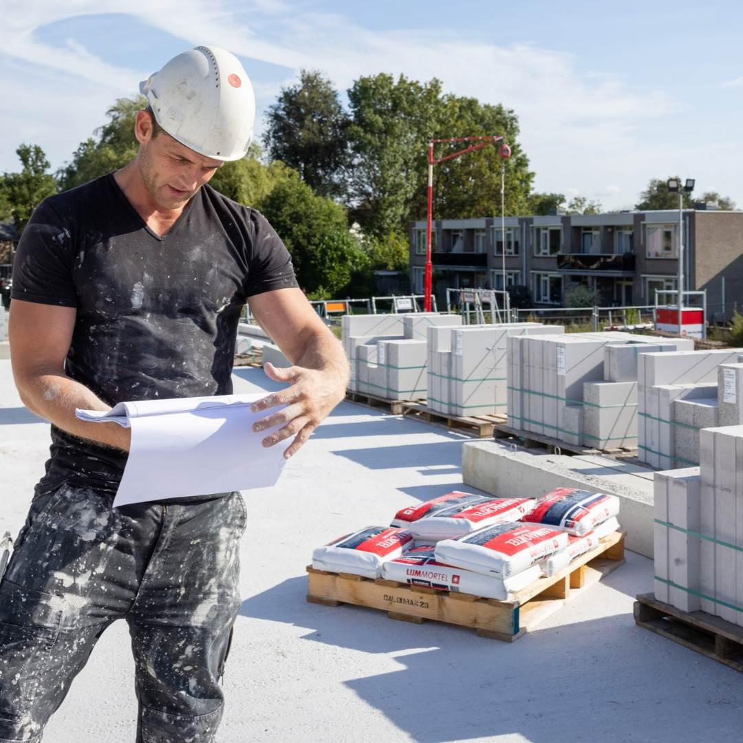 Man, verwerker, op bouwplaats leest wandenboekje voor het verwerken van kalkzandsteen complete bouwpakket.