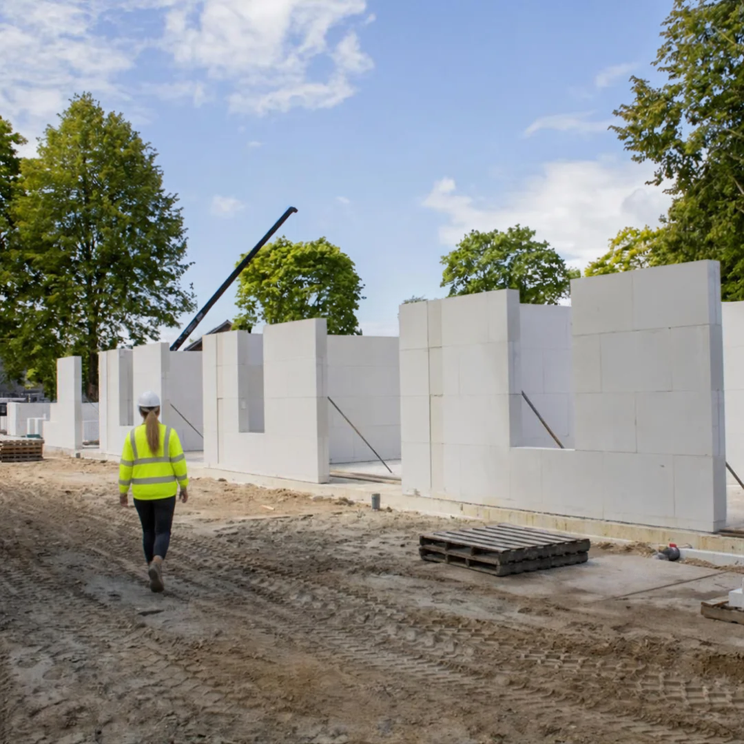 Vrouw met bouw werkkleding loopt op bouwplaats richting kalkzandsteencasco.