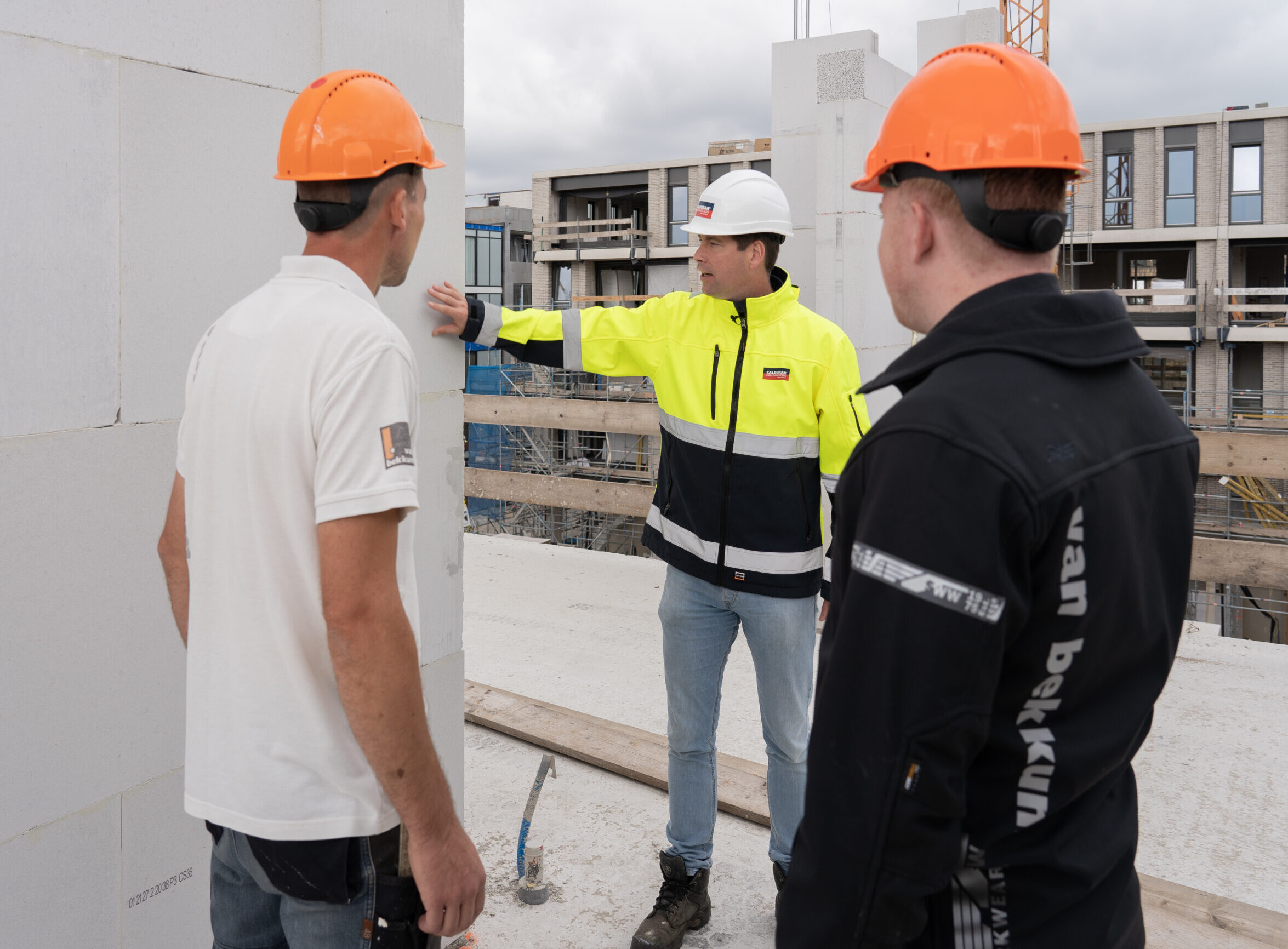 Medewerker Calduran, man, in gesprek met twee mannen van de aannemer op de bouwplaats.