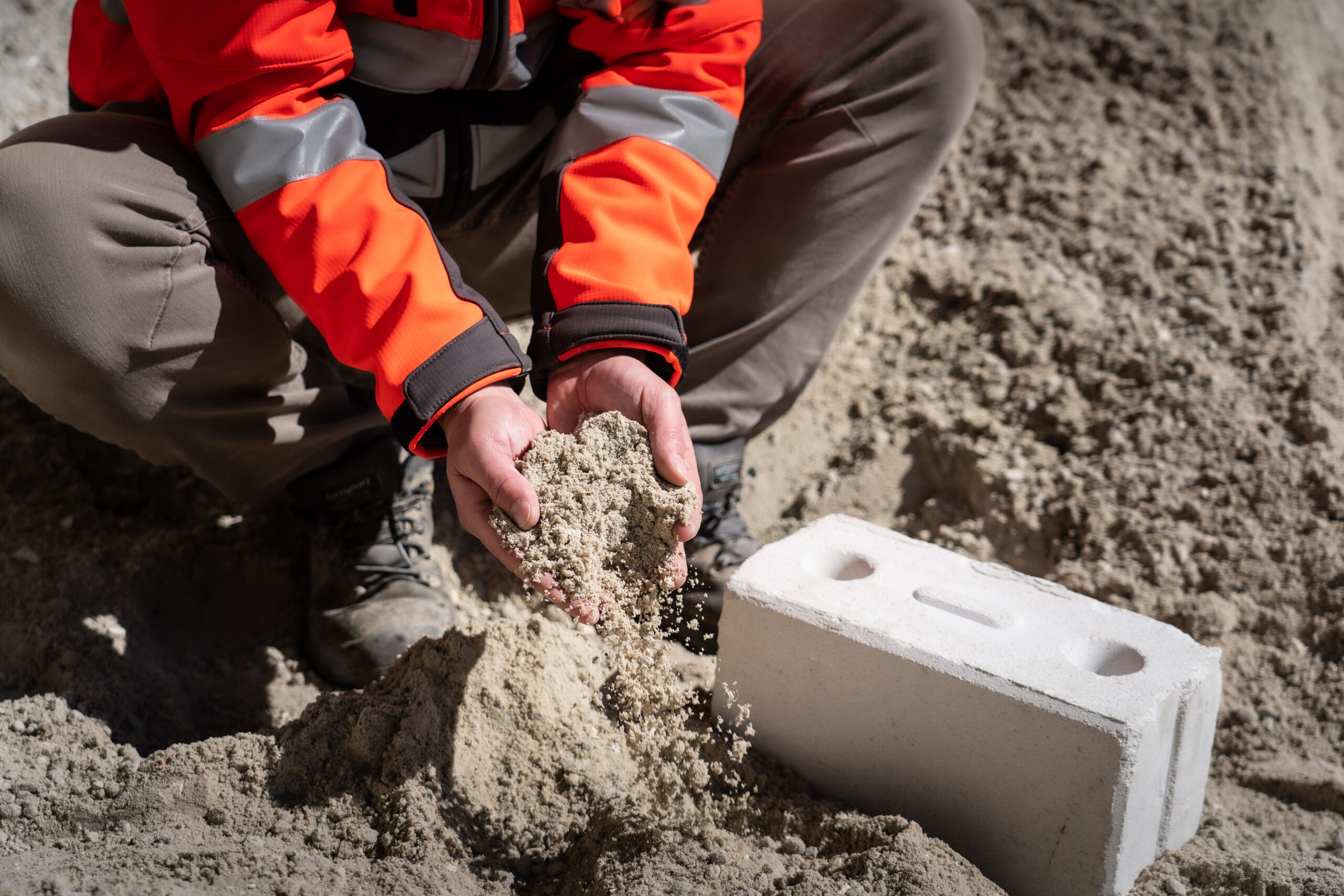 Handen die zand pakken naast duurzaam kalkzandsteen blok.