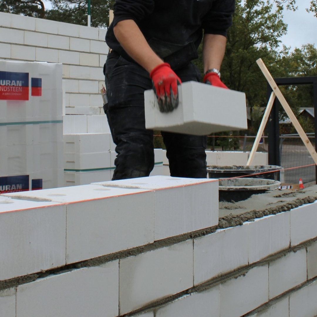 Metselaar metselt een wand met kalkzandsteen metselblokken. Op de achtergrond staat een pakket met verpakking van Calduran.